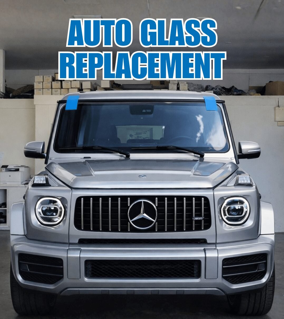 Silver Mercedes G Wagon inside an auto glass and window tint garage with freshly installed windshield and blue installation tape visible.